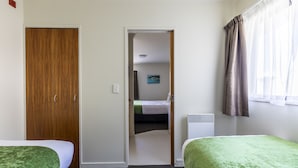A hotel room with two single beds, a wooden wardrobe, a radiator, and a window with curtains. - Bella Vista Motel Wellington (Wellington)