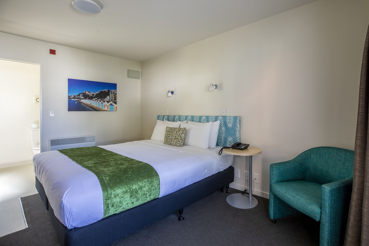 Ein Hotelzimmer mit einem Bett, einem Sessel, einem kleinen Tisch und einem Bild an der Wand.