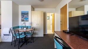 A compact room with a dining table, chairs, a flat-screen TV, and a wooden wardrobe. - Bella Vista Motel Wellington (Wellington)