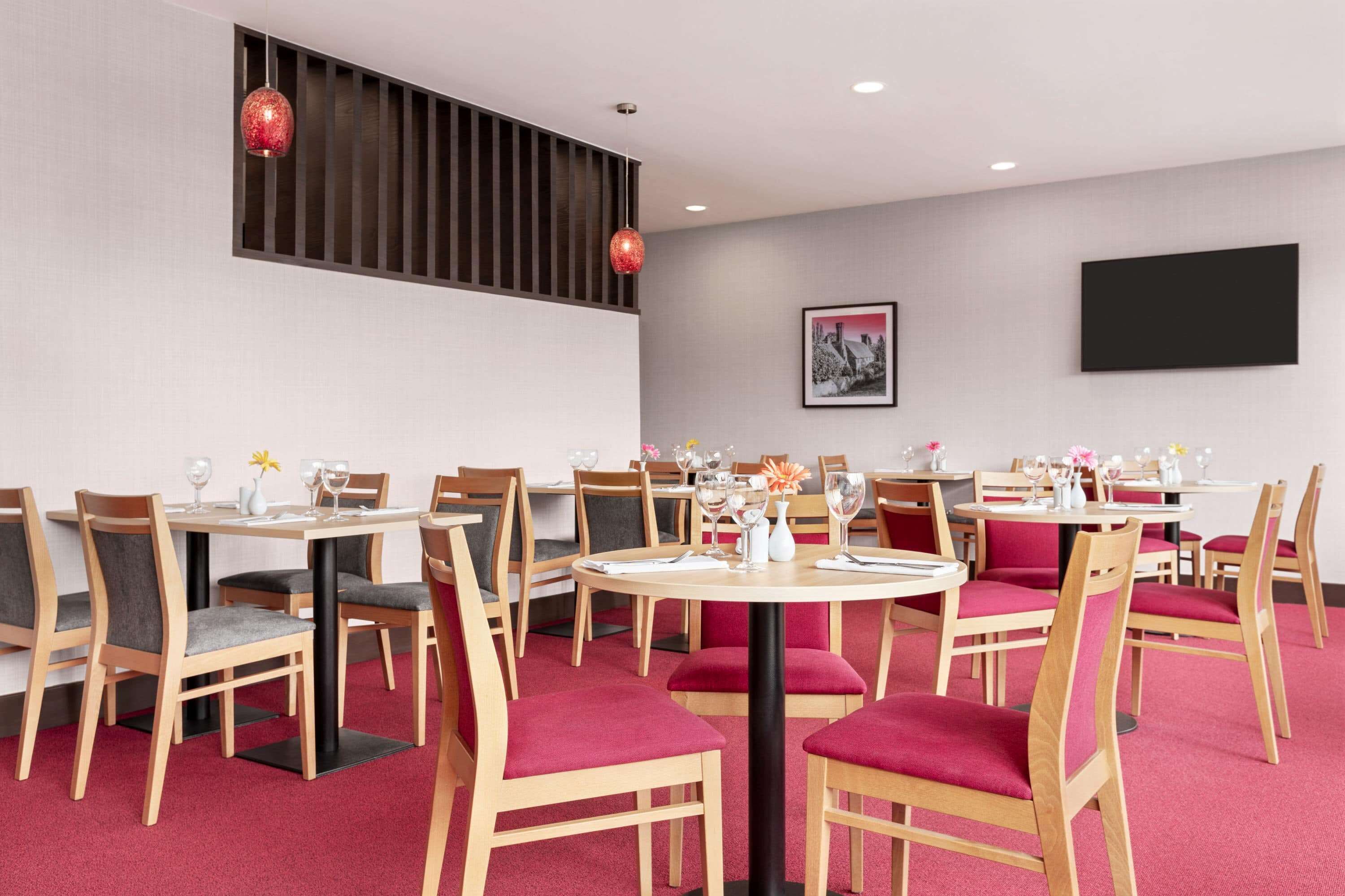 A restaurant with round tables and chairs, some with red cushions.