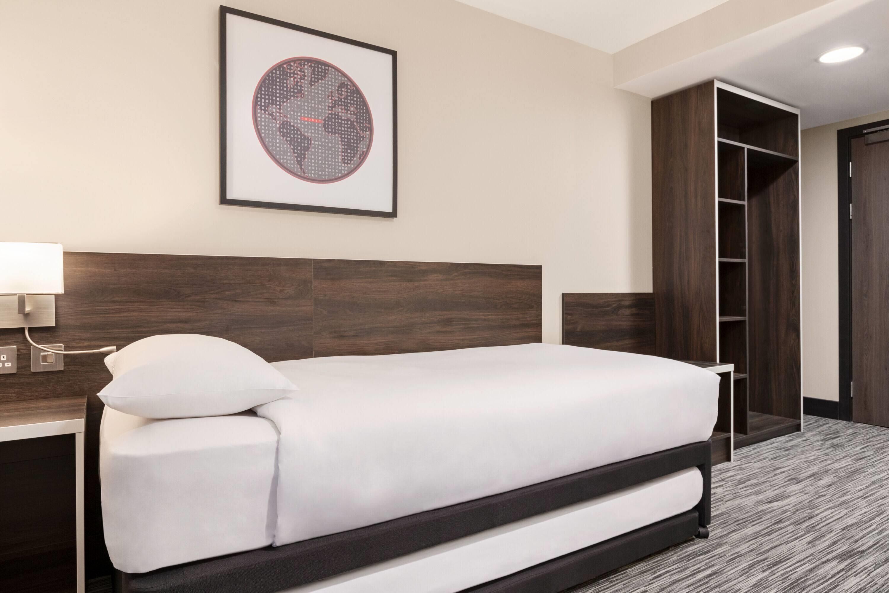 Une chambre d’hôtel avec un lit, un tableau encadré au mur, une table de chevet, une lampe et une armoire.