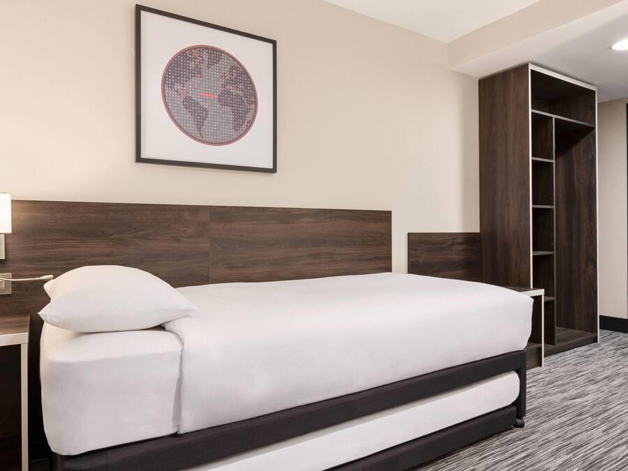 Une chambre d’hôtel avec un lit, un tableau encadré au mur, une table de chevet, une lampe et une armoire.