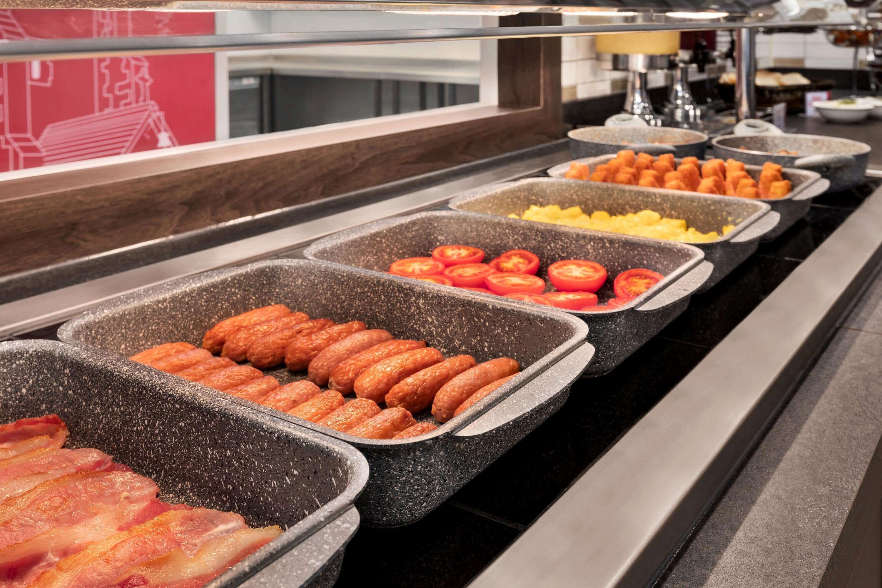 A buffet with various food items including sausages, bacon, tomatoes, and other prepared dishes.