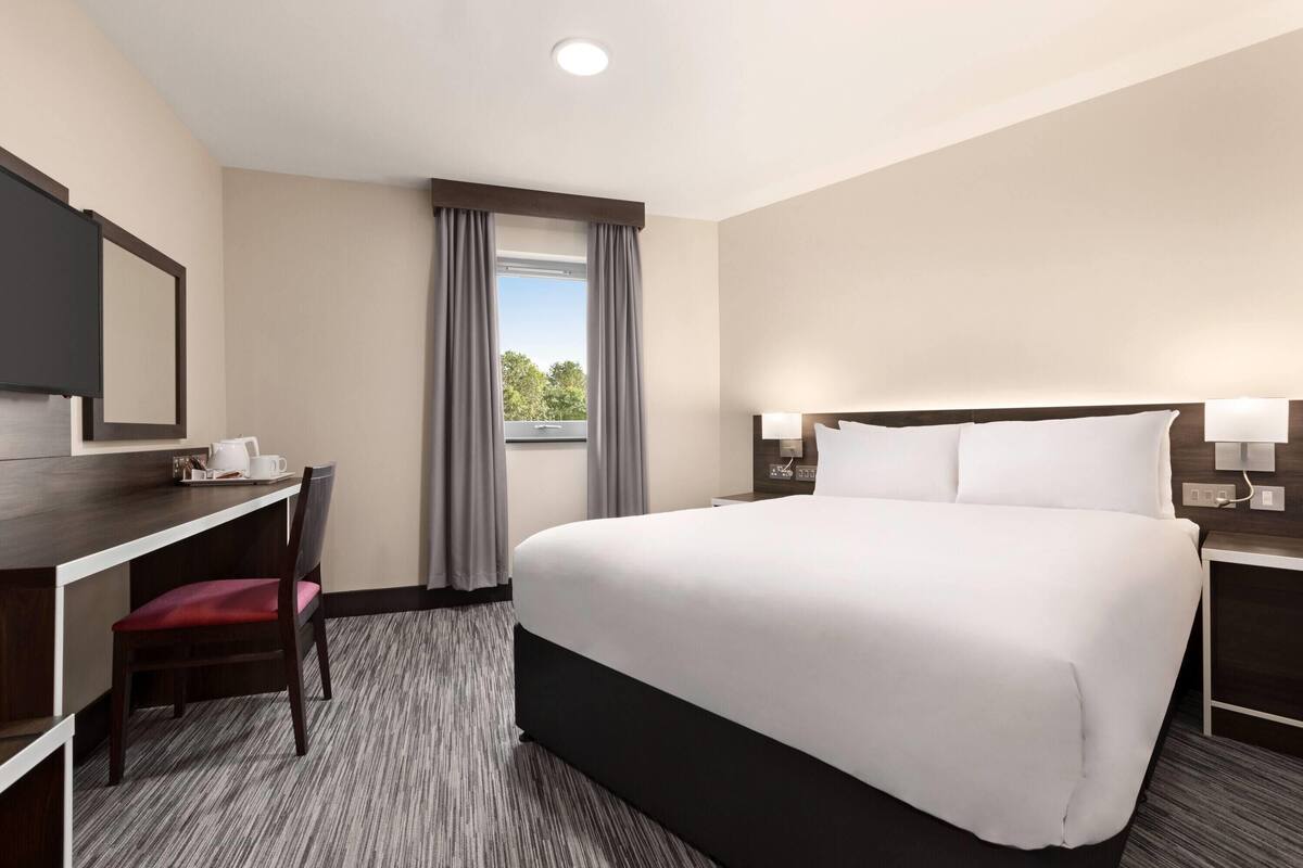 A hotel room with a bed, desk, chair, and a window with curtains.