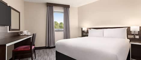 A hotel room with a bed, desk, chair, and a window with curtains.