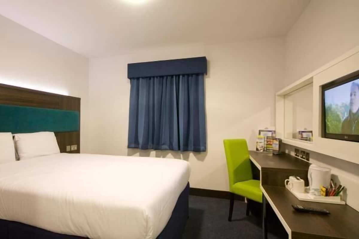 A hotel room with a bed, a desk, a chair, a television, and a window with curtains.