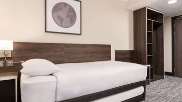 A neatly made bed in a hotel room with a wooden headboard, a framed picture on the wall, and a closet with a mirror.
