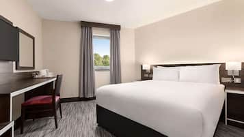Habitación de hotel con cama, escritorio con silla, ventana con cortinas y mesita de noche con lámpara.