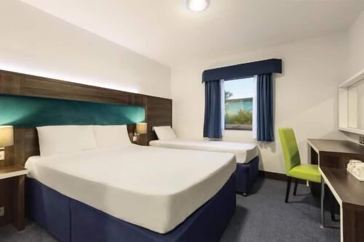 A hotel room with a large bed, a desk, a chair, and a window with curtains.