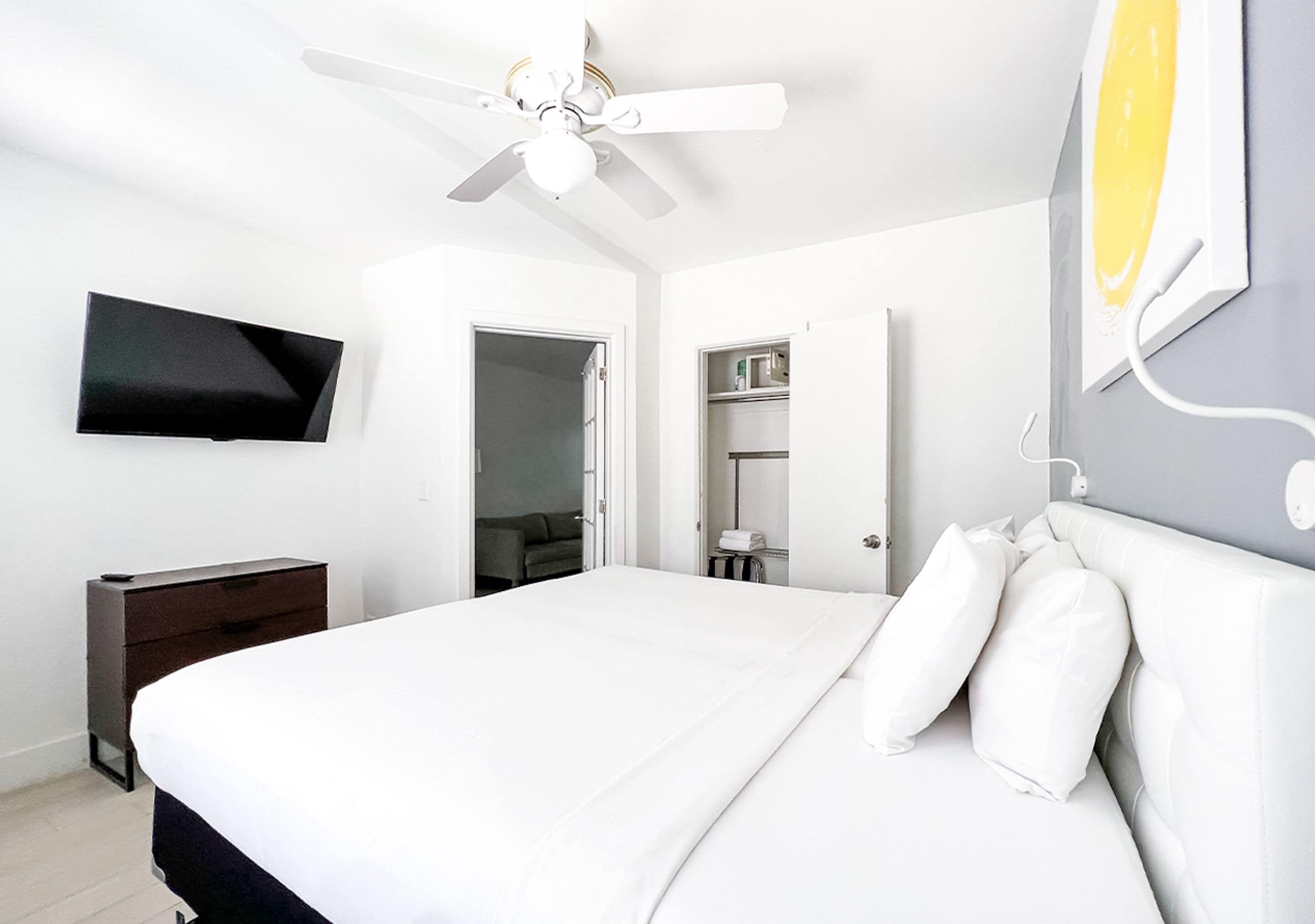 Een moderne hotelkamer met een groot bed, een plafondventilator, een flatscreen televisie aan de muur en een garderobe met spiegel.