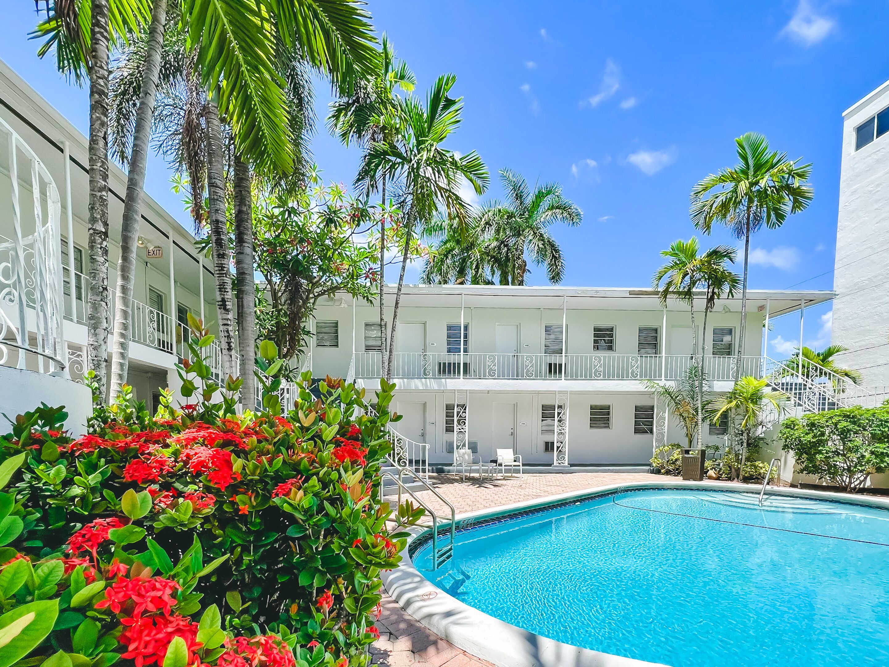 A pool area with a clear blue pool, surrounded by lush greenery and palm trees.