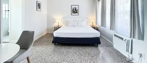 Une chambre d’hôtel comprenant un lit, deux tables de chevet avec des lampes, une chaise, une table, un ventilateur de plafond et une fenêtre avec des rideaux.