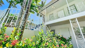 Un bâtiment à deux étages doté d’un balcon, entouré d’une végétation luxuriante et de plantes en fleurs.
