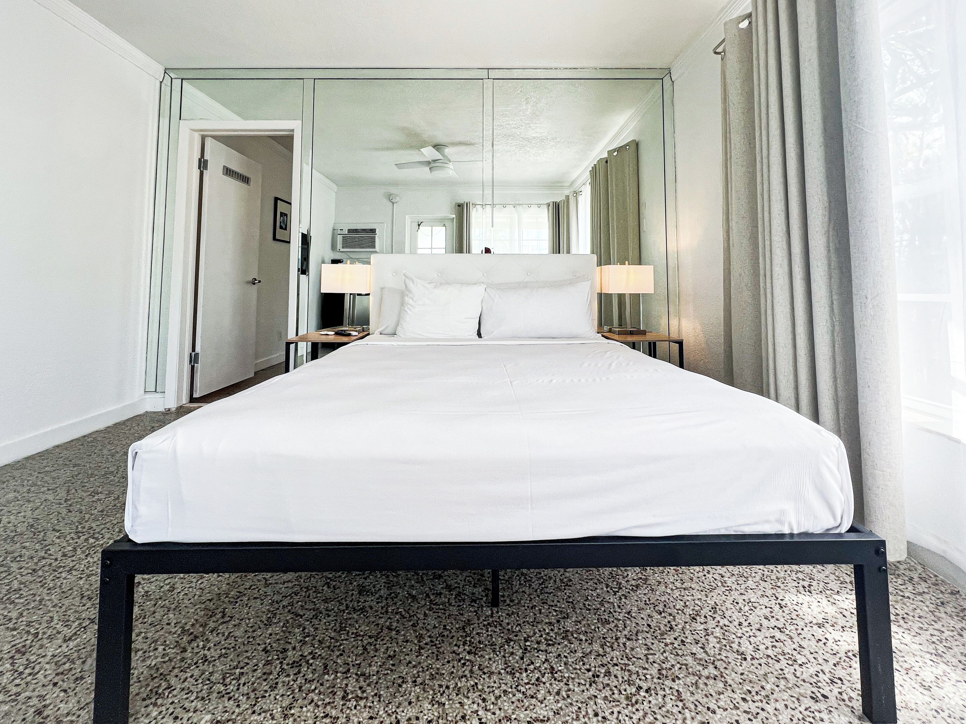 A large bed with white linens, a ceiling fan, and a view of a hallway with a door.