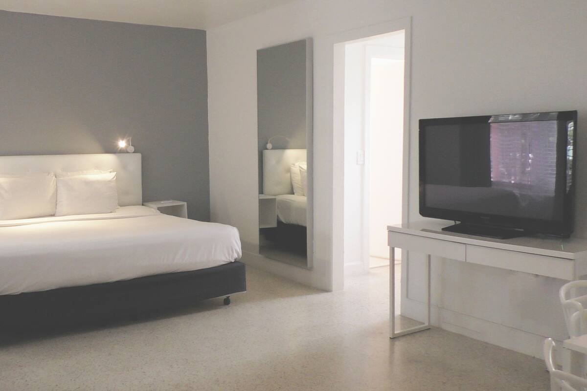 Une chambre à coucher moderne avec un lit, des tables de chevet, un téléviseur et un miroir.