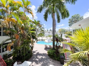 Une piscine entourée de palmiers, un bâtiment blanc et un ciel d’un bleu limpide.