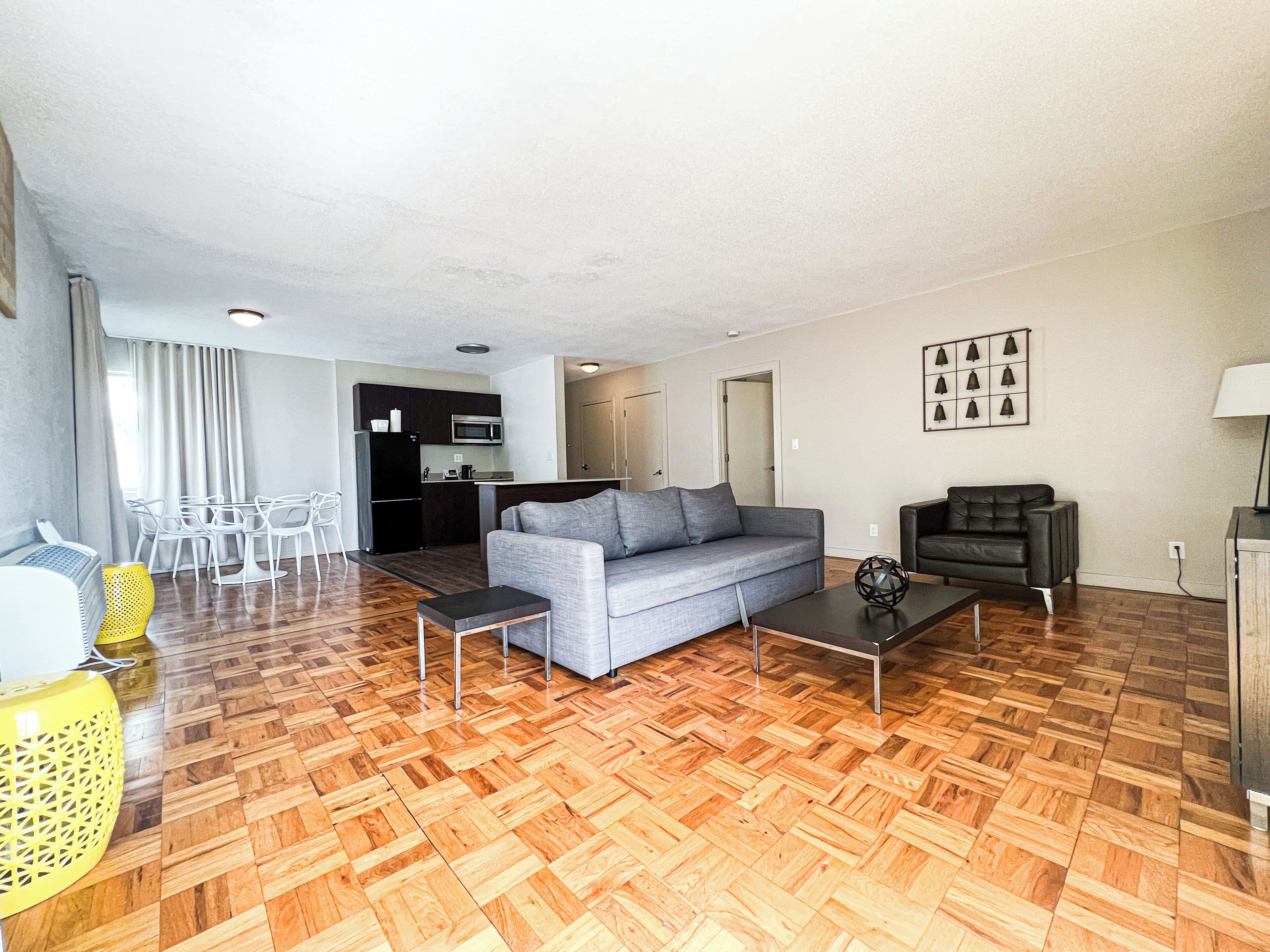 A modern living room with a grey sofa, a coffee table, and a dining area with white chairs.