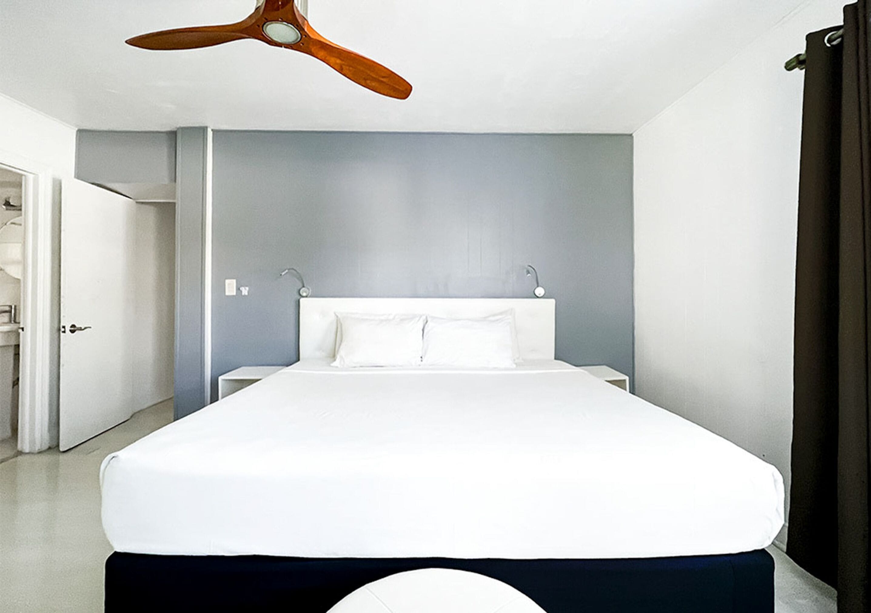 Una habitación de hotel con una cama grande, un ventilador de techo y una puerta que da a otra estancia.