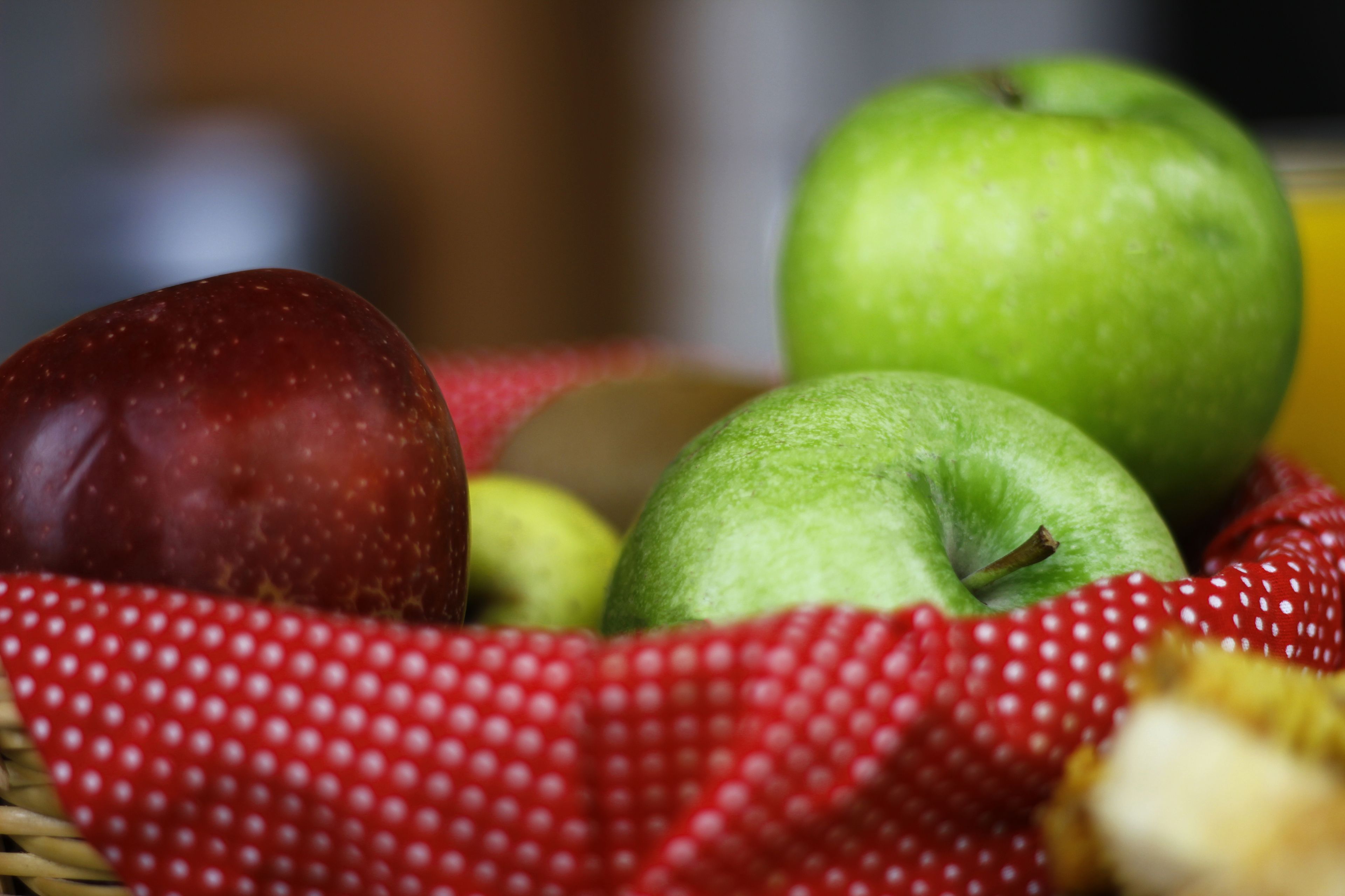 A basket containing red and green apples, a strawberry, and a banana.