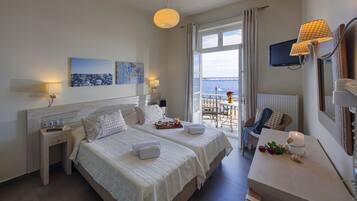 Une chambre d’hôtel avec deux lits, un bureau, une chaise, une télévision et un balcon donnant sur la mer.