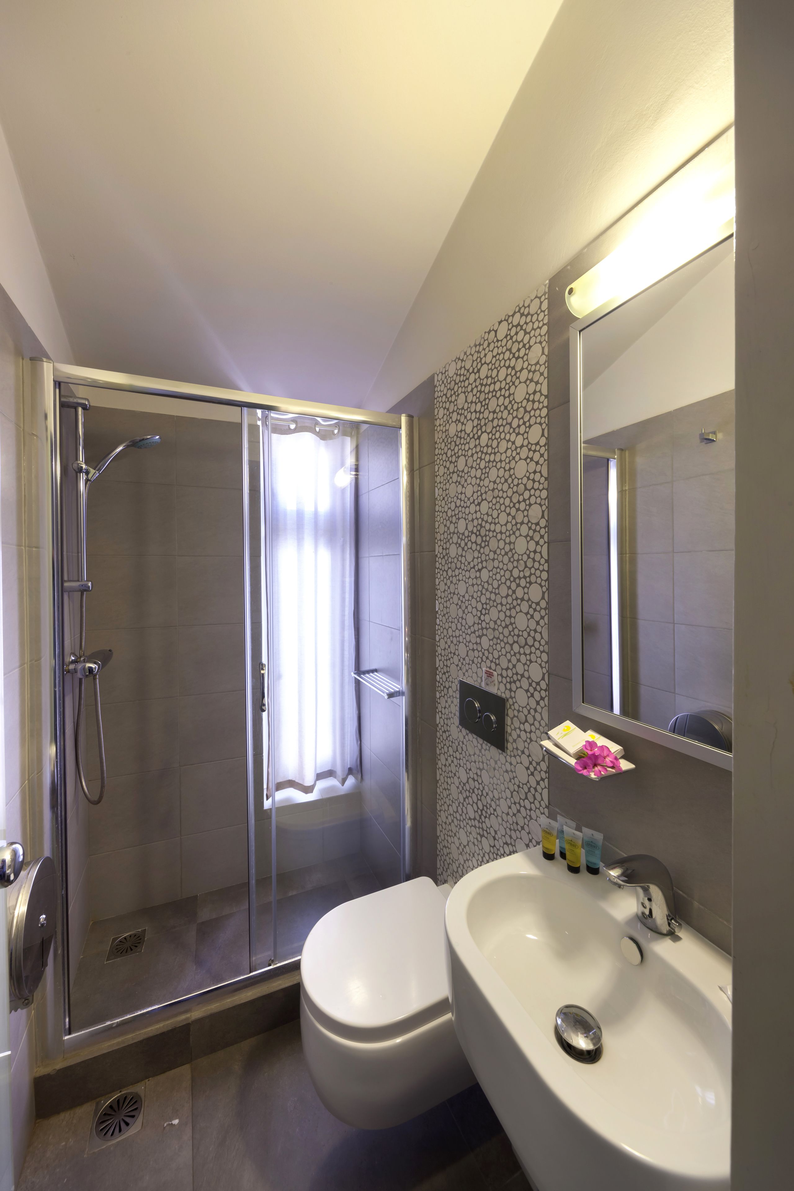 A modern bathroom with a glass-enclosed shower, a white toilet, and a sink with a mirror above it.