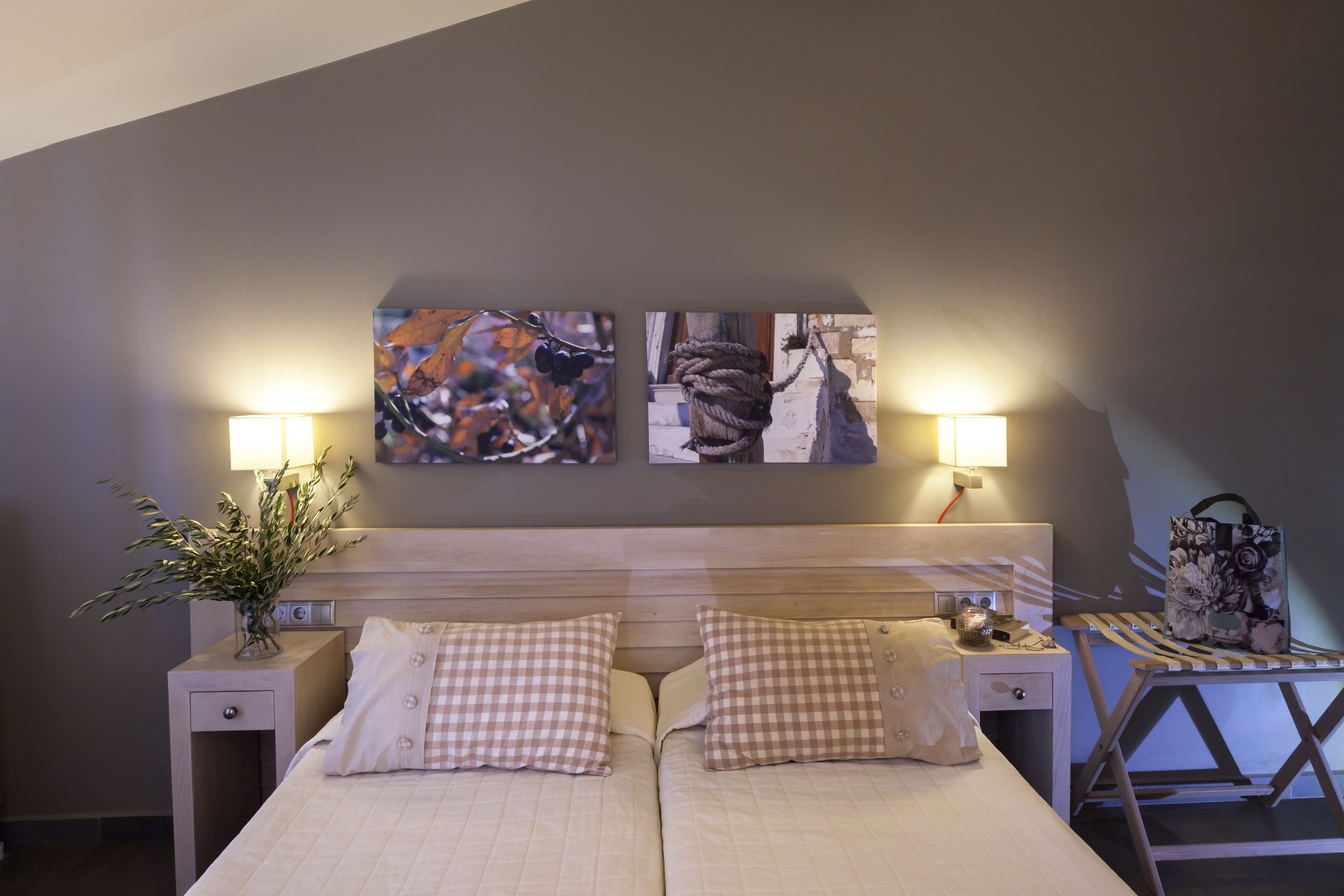 Un lit double avec des coussins à carreaux, une table de chevet avec une lampe et une œuvre d’art accrochée au mur.