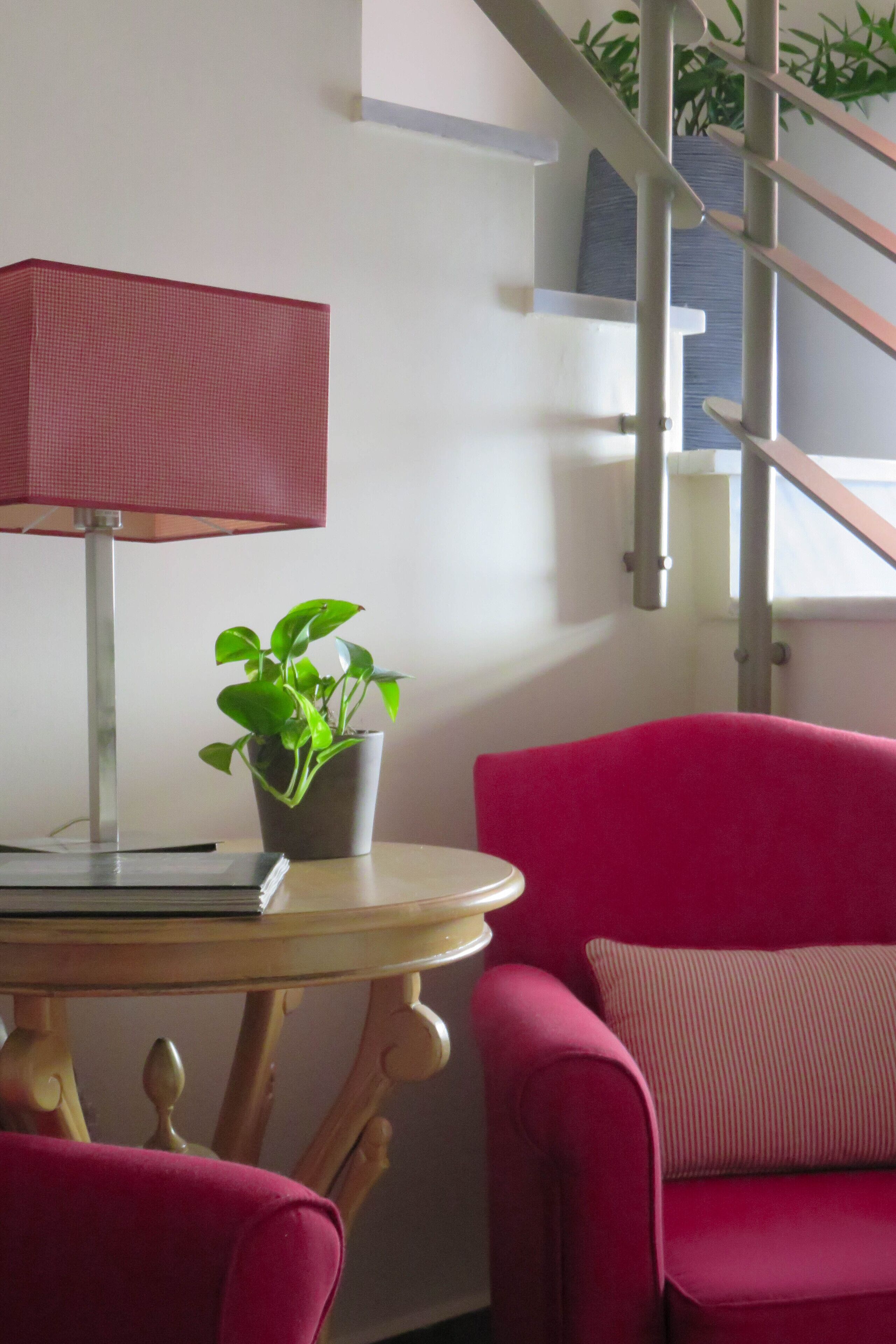 Una habitación con una mesa redonda de madera, un sillón rojo, un sofá rojo, una planta en maceta y una lámpara roja.