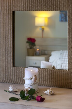 A candle with seashells and a rose on a table, with a mirror reflecting a room.