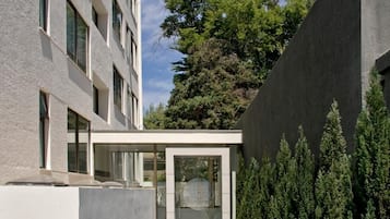 Un edificio moderno con un paseo cubierto, una entrada de vidrio y una fila de árboles perennes.