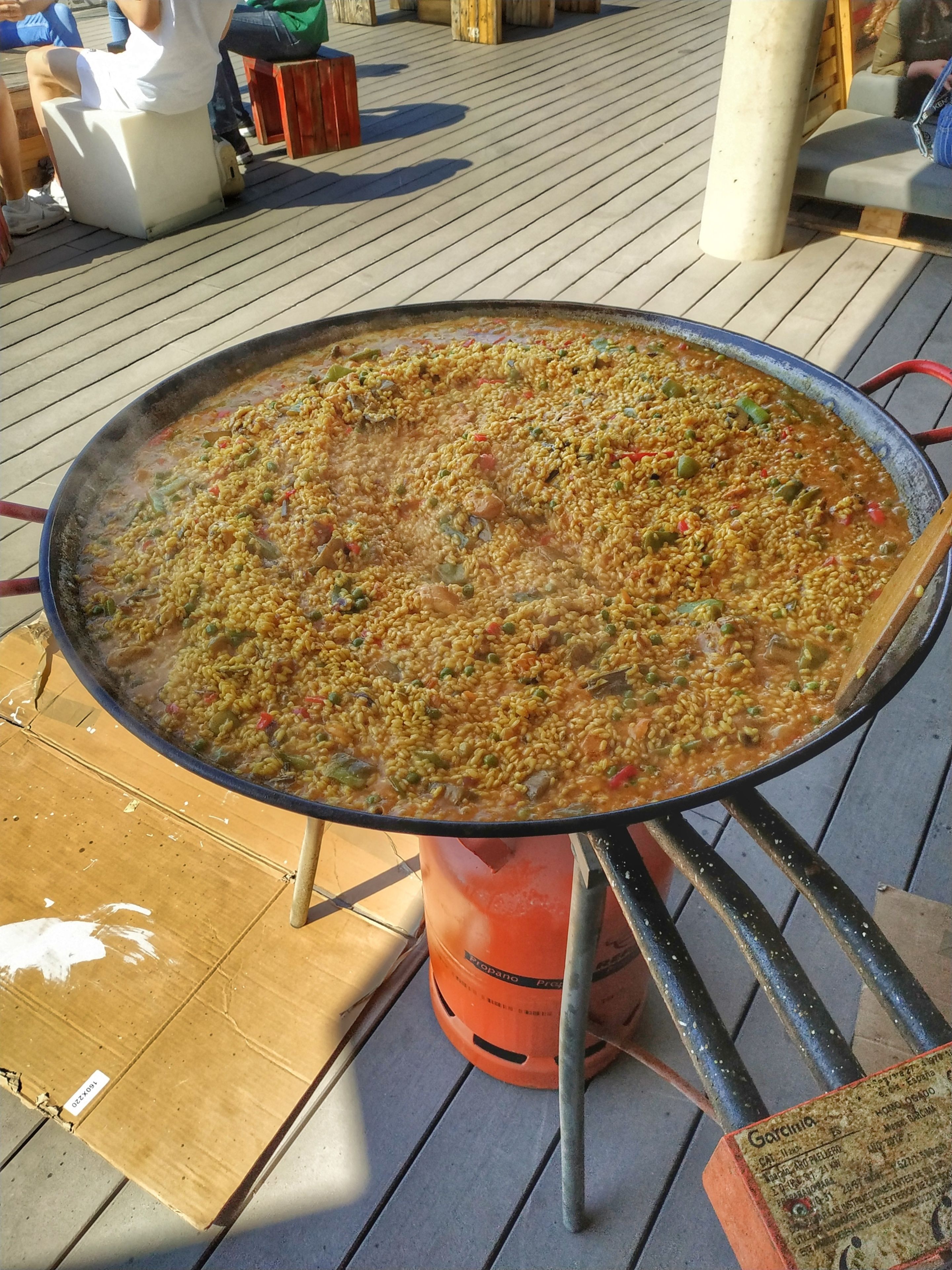 Una olla grande para cocinar al aire libre, llena de un plato de arroz, sobre un fogón de gas portátil.