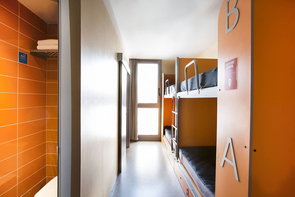A narrow corridor with bunk beds labeled A and B, a window with curtains, and a towel rack.