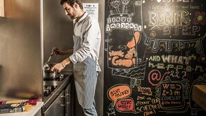 Un chef cocinando en una cocina con una pared de pizarra que muestra varios mensajes y dibujos.