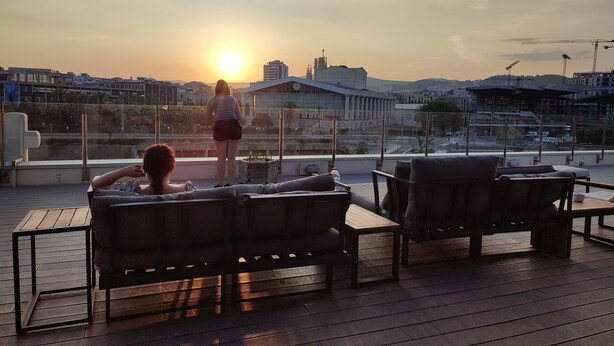 Una terraza en la azotea con dos sillones de relax, una persona de pie y vistas al atardecer.