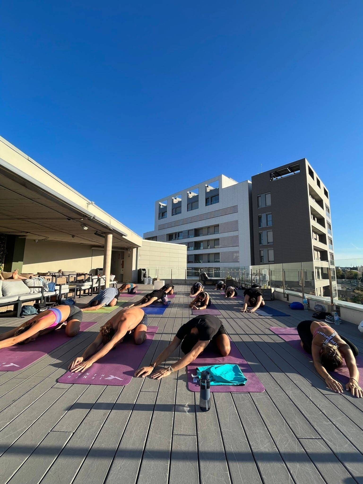 En grupp människor som utövar yoga på ett trädäck med en byggnad i bakgrunden.