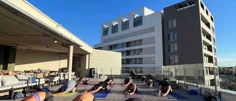 A group of people doing yoga on a wooden deck with a building in the background.