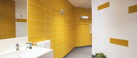 Un baño con azulejos amarillos y blancos, un lavamanos blanco y una planta en maceta.