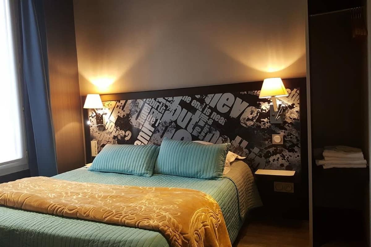 A hotel room with a bed, two bedside lamps, a window with curtains, and a wall with text and graphics.