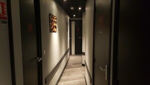A narrow hallway with a light-colored floor, a wall-mounted artwork, and a door at the end. - Café hôtel de l'Avenir (Saint-Ouen)