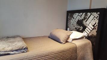 Ein ordentlich bezogenes Bett mit einer beigen Steudecke, einer gefalteten Decke und zwei Kissen.