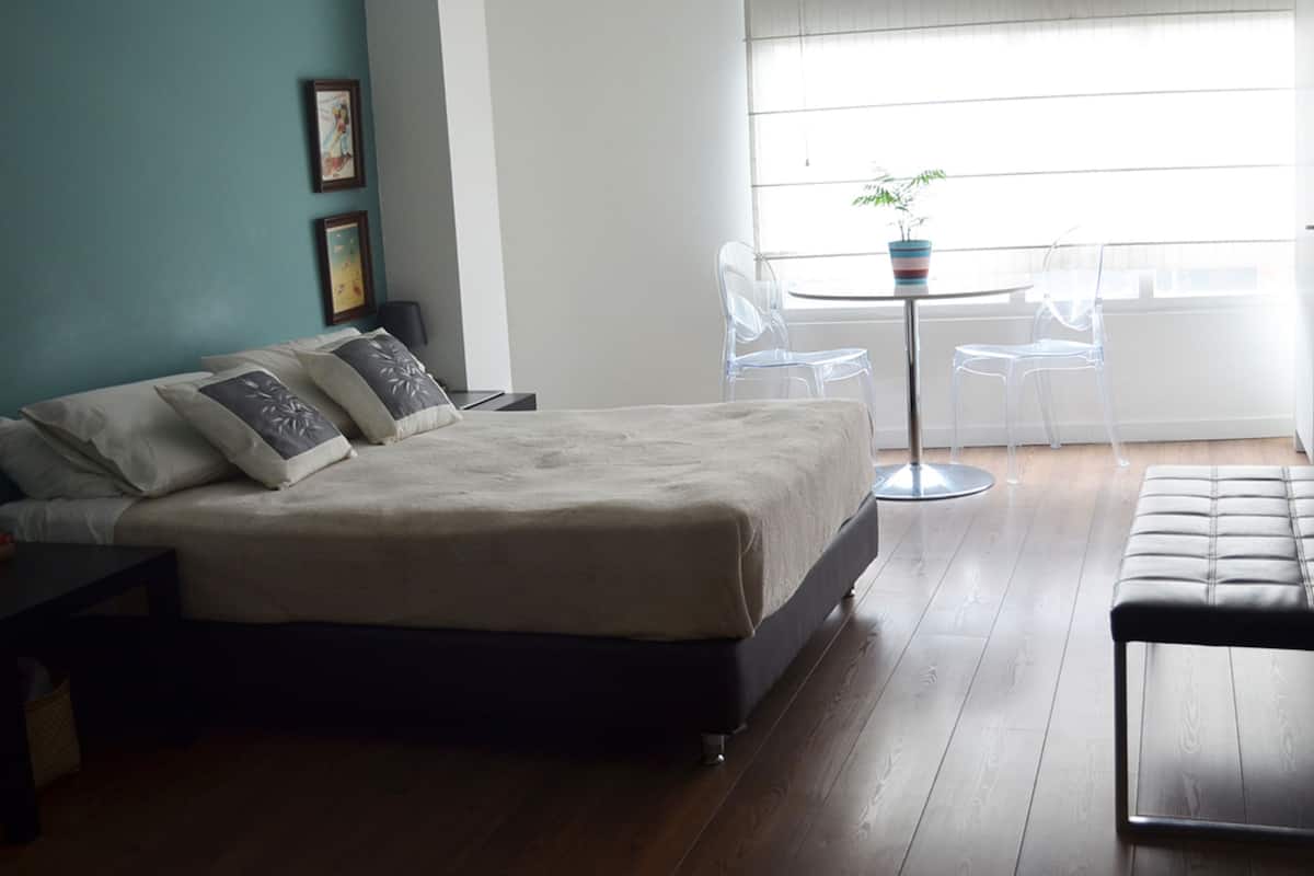 A bedroom with a bed, bedside tables, a small table with chairs, and a window with blinds.