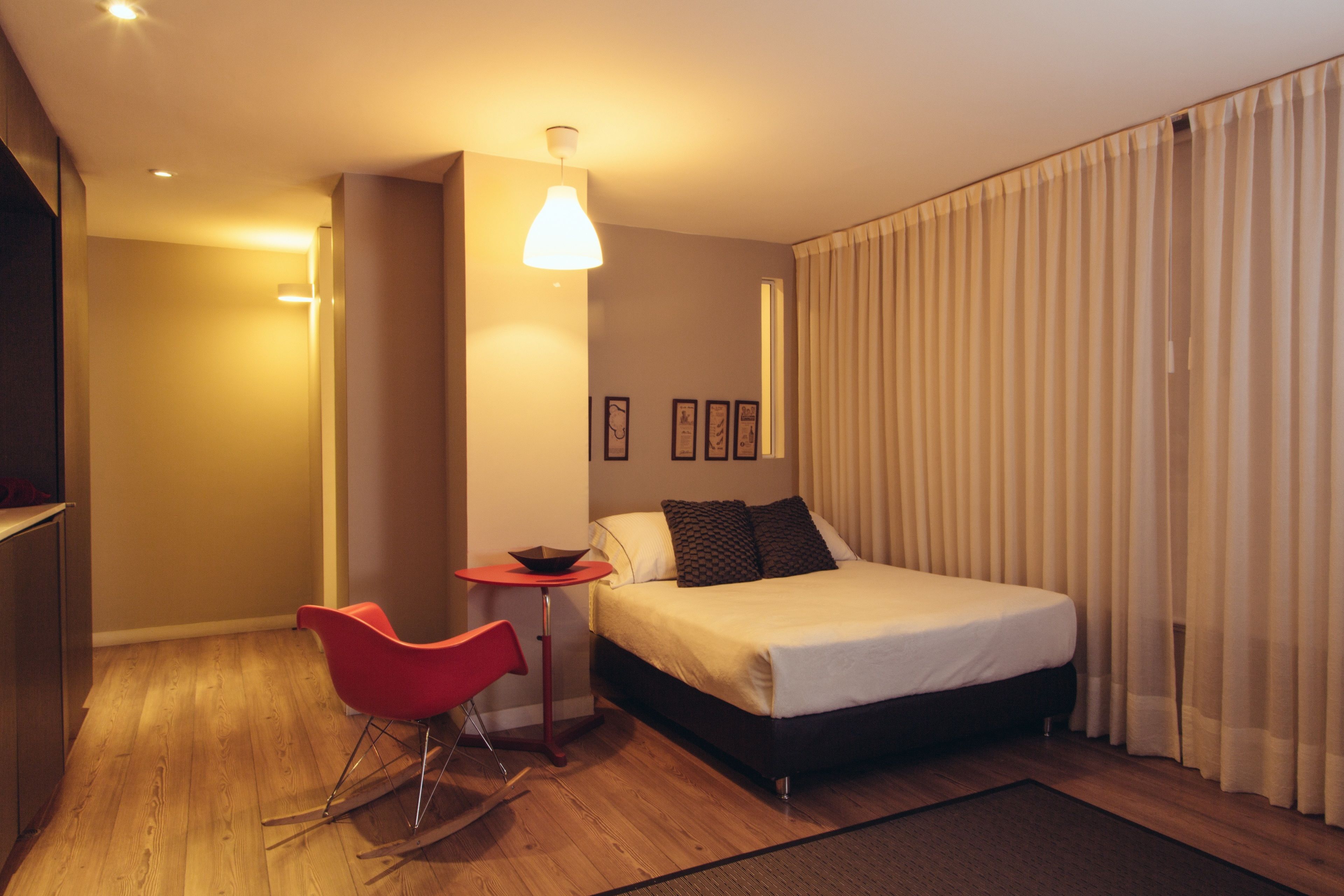 A modern hotel room with a bed, a red chair, a small table, and a ceiling light.
