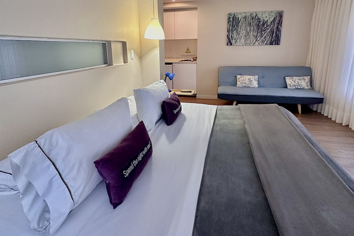 A hotel room with a bed, a desk, a chair, a painting, and a window.
