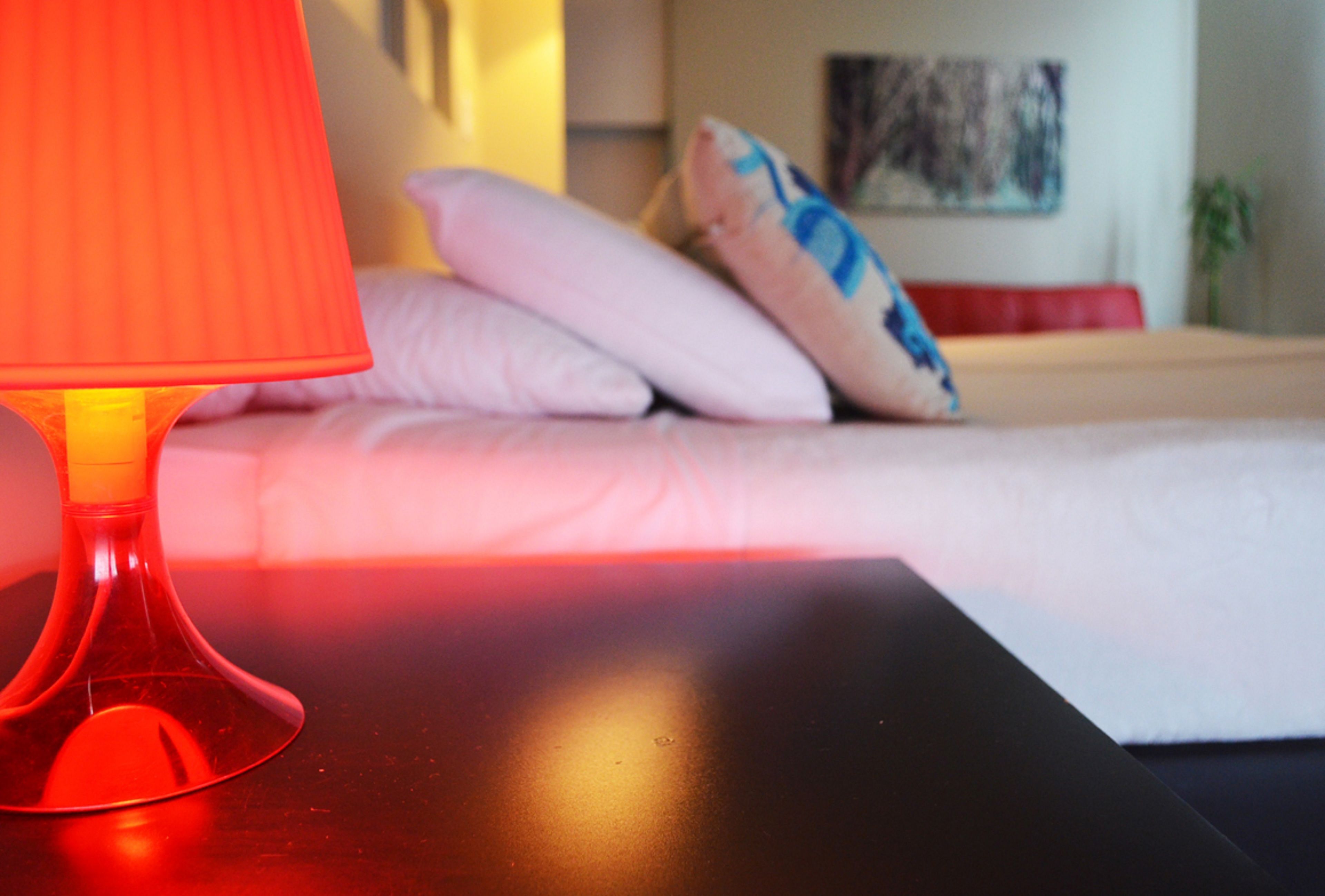 Ein Bett mit weißer Bettwäsche und einer roten Lampe auf schwarzer Oberfläche.