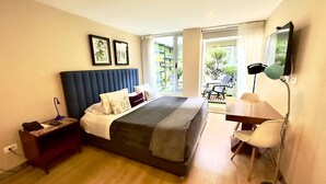 A modern bedroom with a large bed, a desk, and a chair. There is a window with a view of greenery outside. - Hotel Living 55 (Bogotá)