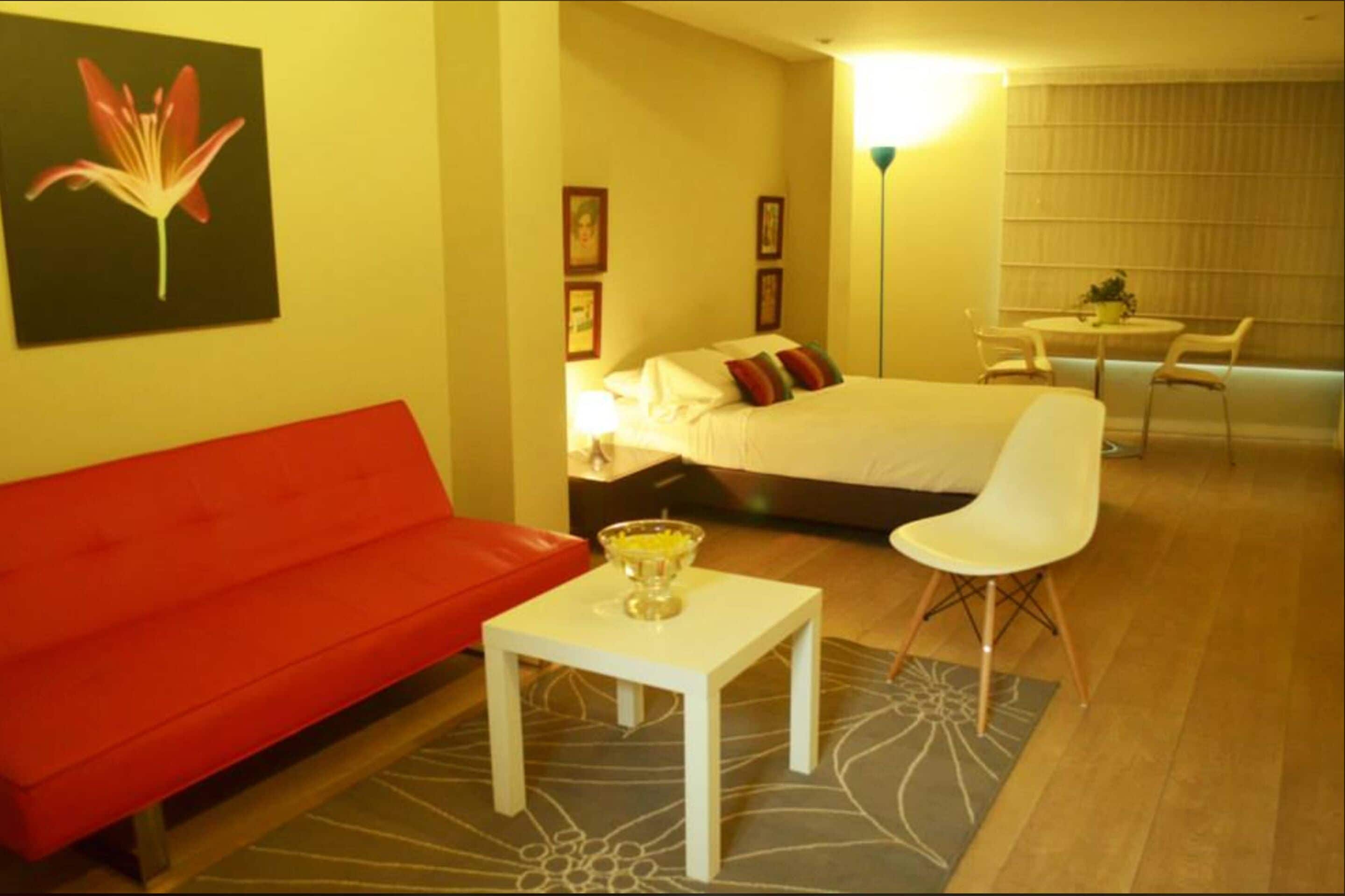 Una habitación de hotel con una cama, un sofá rojo, una mesita con un cuenco y una silla.