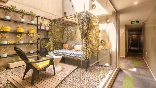 A modern interior with a seating area featuring a bench and a chair, surrounded by potted plants and a hanging garden structure. - Hotel Living 55 (Bogotá)
