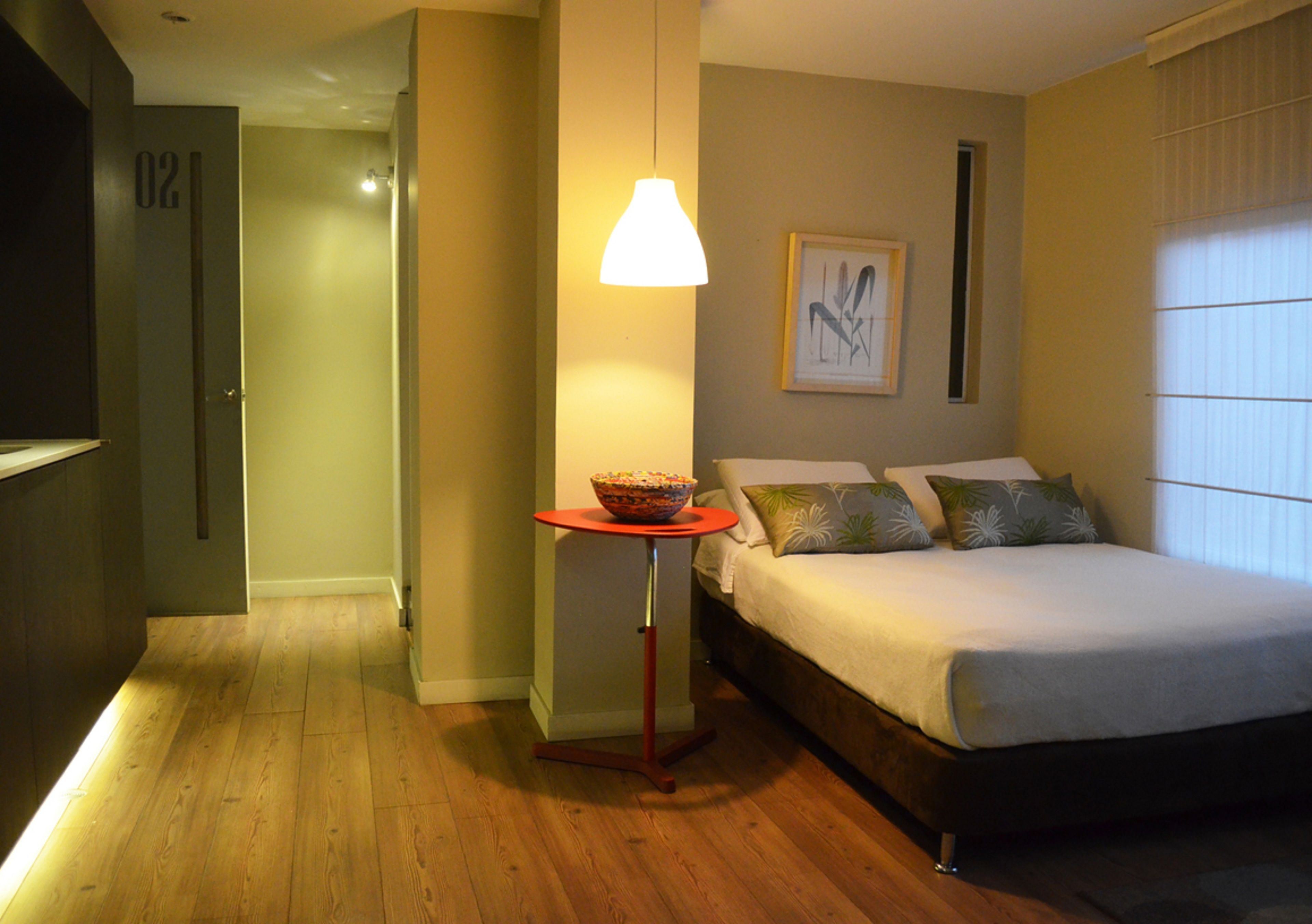Une chambre d’hôtel avec un lit, une petite table sur laquelle se trouve un bol, une lampe et un tableau encadré accroché au mur.