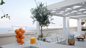 A terrace with a wicker table, a glass pitcher of orange juice, a glass of water, a white sofa, and a small tree. - JR Hotels Bari Grande Albergo delle Nazioni (Bari)