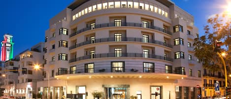 A multi-story hotel with a curved facade, multiple balconies, and a ground-level entrance with a glass door.