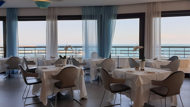 A restaurant with tables set for dining, large windows with ocean views, and blue curtains. - JR Hotels Bari Grande Albergo delle Nazioni (Bari)